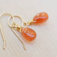 Genuine orange sunstone teardrop dangle earrings shown in 14k gold filled. The gemstones are smooth polished. Close up image showing the shimmer within the stone.
