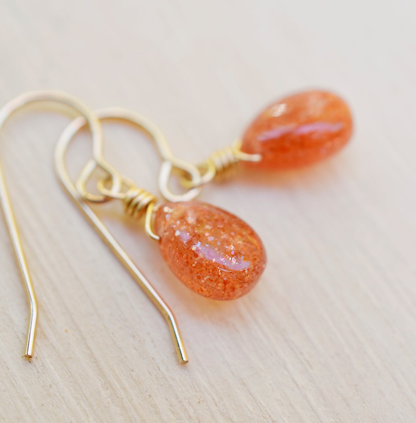 Genuine orange sunstone teardrop dangle earrings shown in 14k gold filled. The gemstones are smooth polished. Close up image showing the shimmer within the stone.