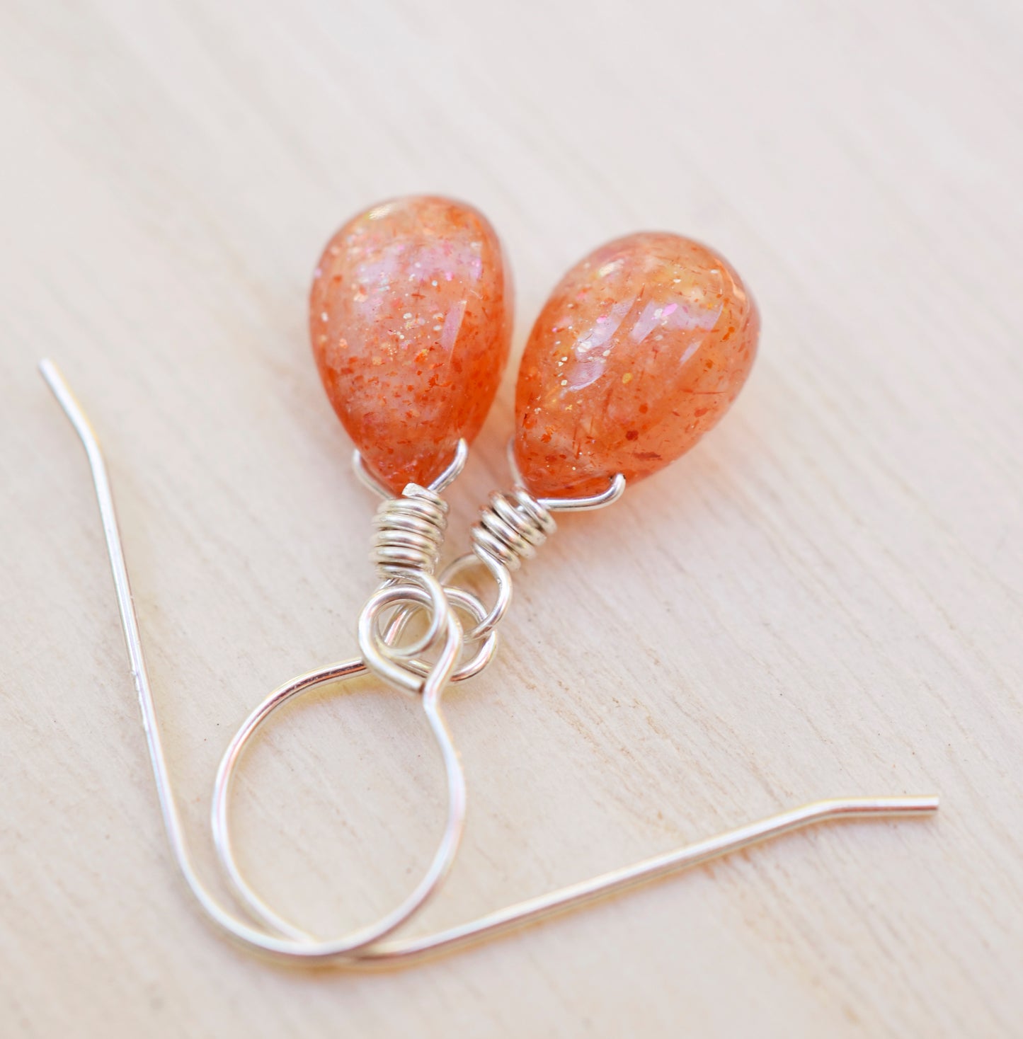 Genuine orange sunstone teardrop dangle earrings shown in sterling silver. The gemstones are smooth polished.