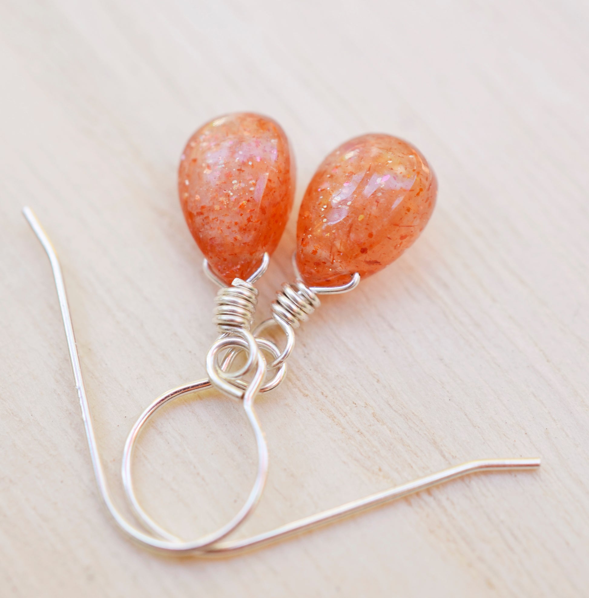 Genuine orange sunstone teardrop dangle earrings shown in sterling silver. The gemstones are smooth polished.
