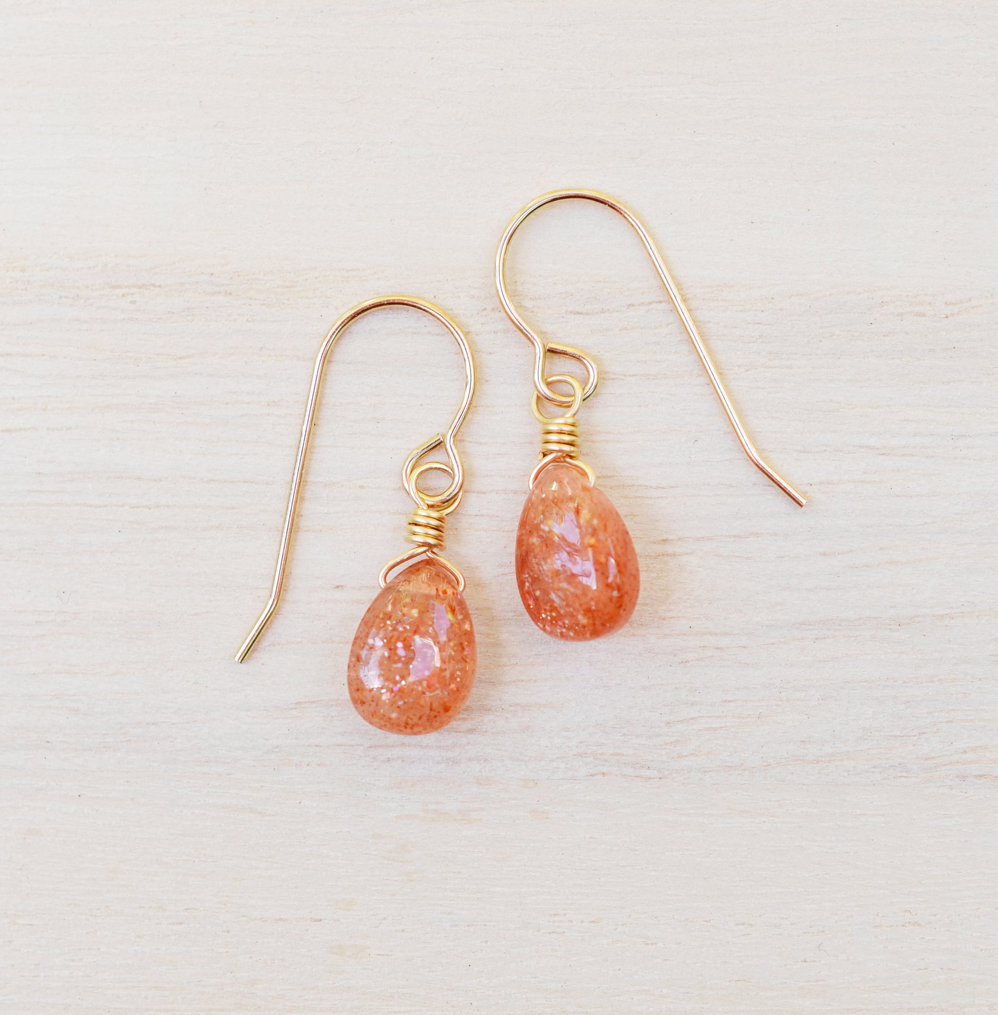Genuine orange sunstone teardrop dangle earrings shown in 14k gold filled. The gemstones are smooth polished.