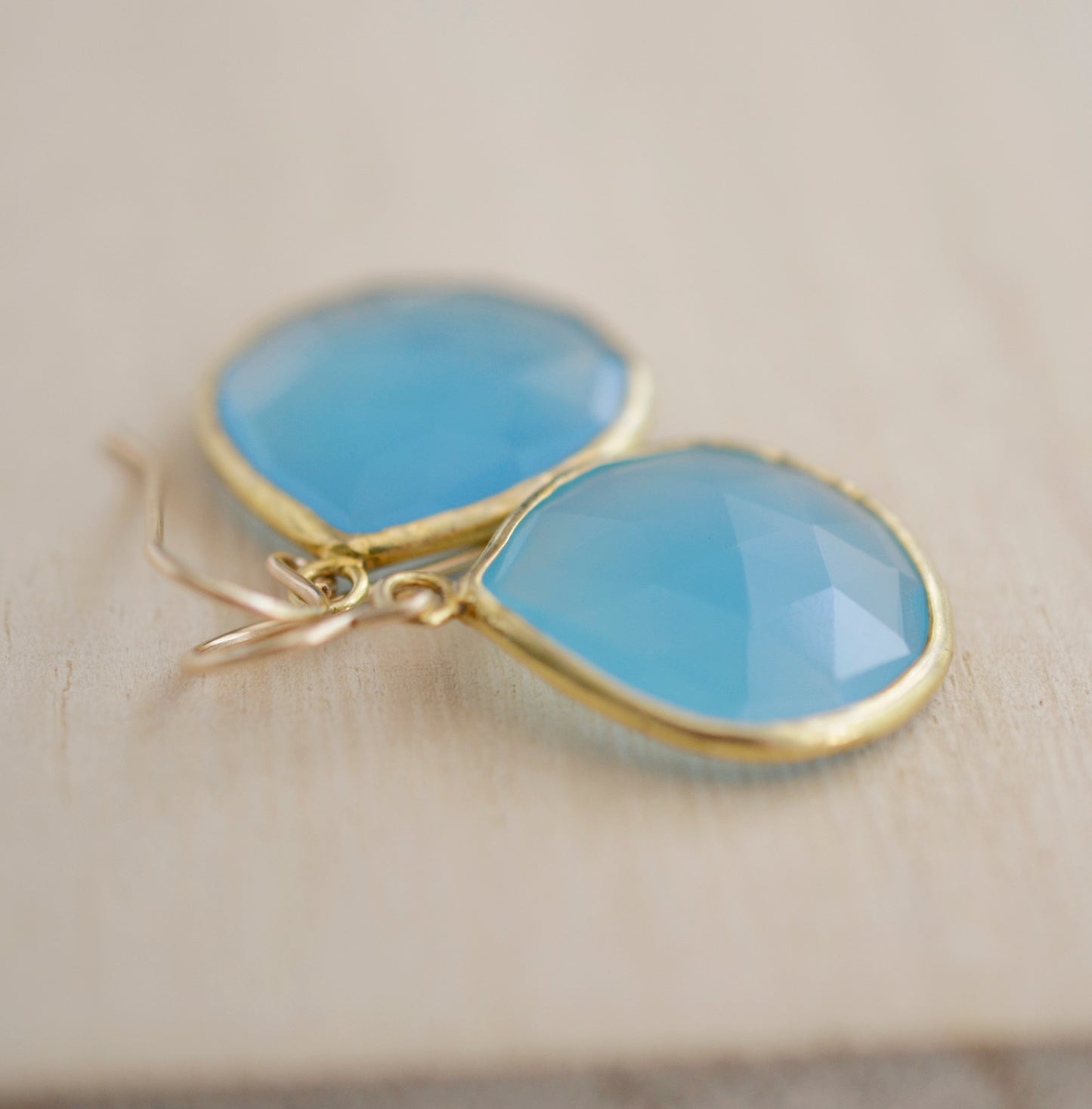 Large blue chalcedony teardrop gemstones bezeled in gold and suspended from earwires. Close up.